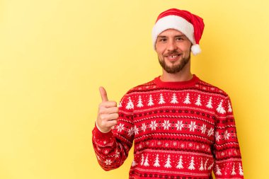 Sarı arka planda izole edilmiş genç beyaz adam gülümsüyor ve başparmağını kaldırıyor.