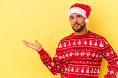 Genç beyaz adam, sarı arka planda izole edilmiş bir şekilde Noel 'i kutluyor. Palmiye üzerinde bir fotokopi alanı ve belinde başka bir el tutuyor..