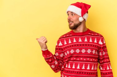 Kafkasyalı genç adam, sarı arka planda izole edilmiş bir şekilde Noel 'i kutluyor. Baş parmak uzakta, gülerek ve kaygısızca..