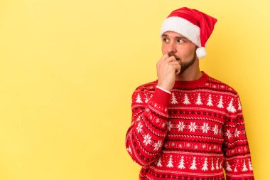 Genç beyaz adam, sarı arka planda izole edilmiş Noel 'i kutluyor. Bir şeyin fotokopi odasına baktığını düşünüyor..