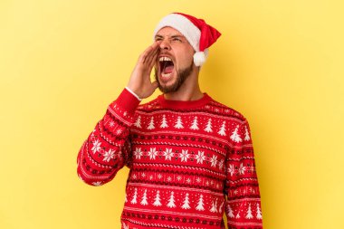 Genç beyaz adam Noel 'i kutluyor sarı arka planda izole edilmiş bağırıyor ve avuç içini açık tutuyor..