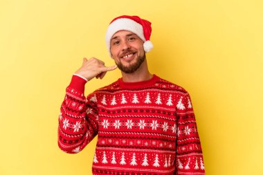 Genç beyaz adam, sarı arka planda izole edilmiş bir şekilde Noel 'i kutluyor. Cep telefonu hareketini parmaklarıyla gösteriyor..