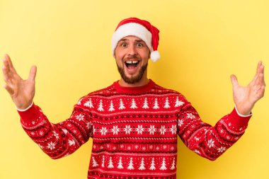 Sarı arka planda izole edilmiş bir şekilde Noel 'i kutlayan beyaz bir genç hoş bir sürpriz alıyor, heyecanlı ve el kaldırıyor..