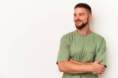 Beyaz arka planda izole edilmiş beyaz tenli genç beyaz adam kollarını kavuşturarak gülümsüyor..