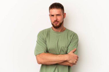 Beyaz arka planda izole edilmiş, hoşnutsuzca kaşlarını çatmış, kollarını kavuşturmuş beyaz tenli genç bir adam..