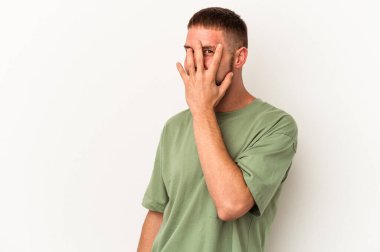 Diastemalı genç beyaz bir adam beyaz arka planda izole edilmiş parmaklarıyla kameraya göz kırpıyor, yüzünü kapatmaktan utanıyor..