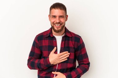 Beyaz arka planda izole edilmiş beyaz tenli genç beyaz adam mutlu bir şekilde gülüyor ve ellerini karnının üstünde tutarak eğleniyor..