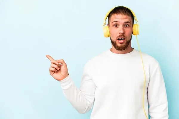 Ung Kaukasisk Man Lyssnar Musik Isolerad Blå Bakgrund Pekar Sidan — Stockfoto