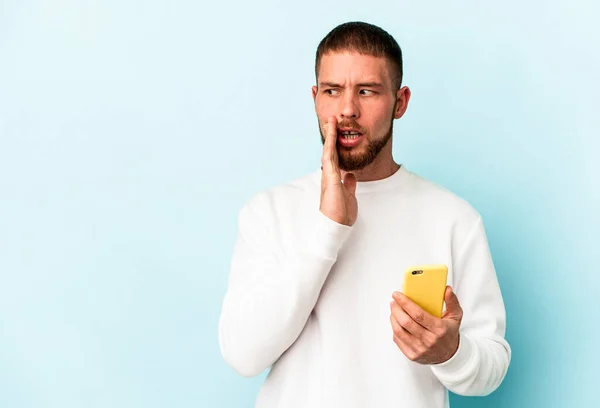 Młody Biały Mężczyzna Trzymając Telefon Komórkowy Odizolowany Niebieskim Tle Mówi — Zdjęcie stockowe
