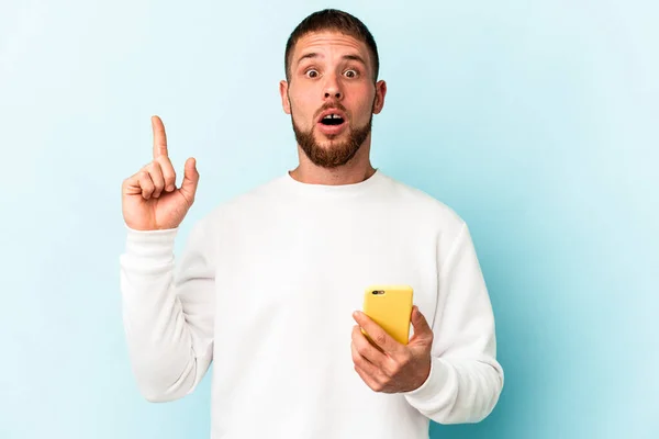 Młody Biały Mężczyzna Trzyma Telefon Komórkowy Odizolowany Niebieskim Tle Mając — Zdjęcie stockowe
