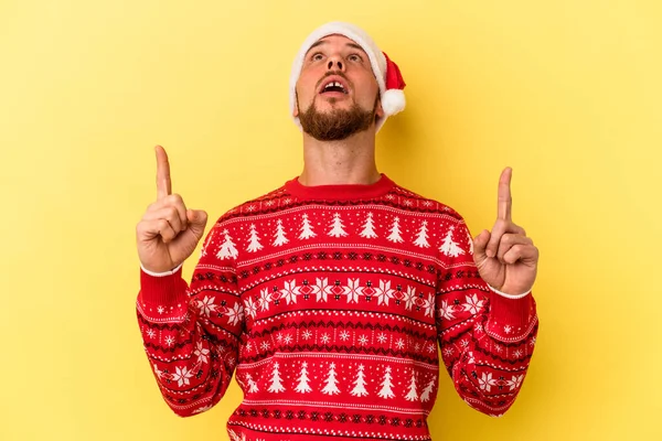 Sarı arka planda izole edilmiş, ağzı açık genç beyaz adam Noel 'i kutluyor..