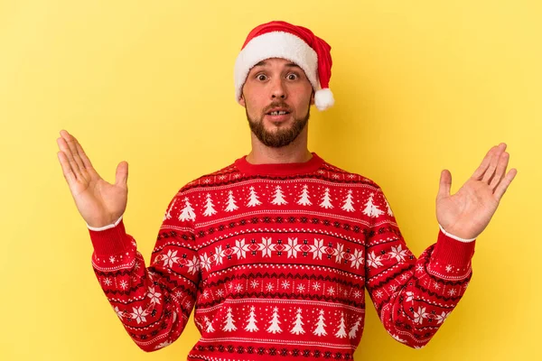 Sarı arka planda izole edilmiş, şaşırmış ve şok olmuş genç beyaz bir adam Noel 'i kutluyor..