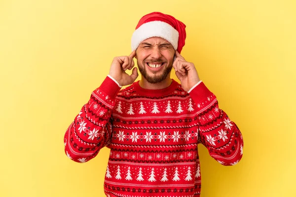 Молодий Кавказький Чоловік Святкує Різдво Ізольовано Жовтому Тлі Покриваючи Вуха — стокове фото