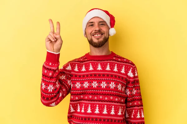 年轻的高加索人在黄色的背景下欢快而无忧无虑地庆祝圣诞节 用手指展示和平的象征 — 图库照片