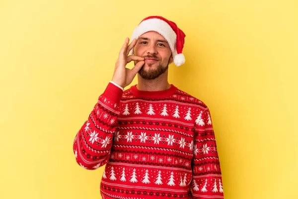 若いですCaucasian男祝いますクリスマス絶縁上の黄色の背景とともに指オン唇維持A秘密 — ストック写真