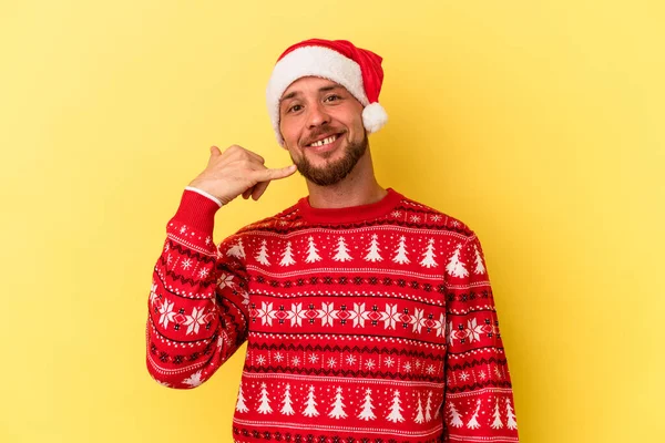 Genç beyaz adam, sarı arka planda izole edilmiş bir şekilde Noel 'i kutluyor. Cep telefonu hareketini parmaklarıyla gösteriyor..