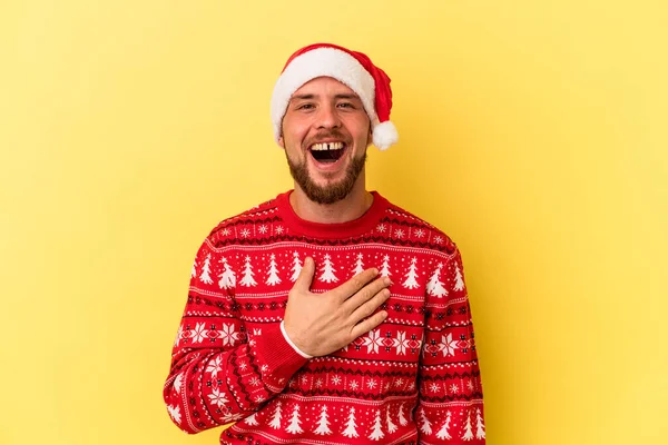 Sarı arka planda izole edilmiş bir şekilde Noel 'i kutlayan Kafkasyalı genç adam elini göğsünde tutarak kahkahalar atıyor..