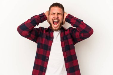 Diastemalı genç beyaz adam beyaz arka planda izole edildi. Kulakları kulaklarla kaplıydı. Çok yüksek ses duymamaya çalışıyordu..