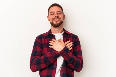 Beyaz arka planda izole edilmiş beyaz tenli genç beyaz adam gülüyor, ellerini kalbe koyuyor, mutluluk kavramını koruyor..