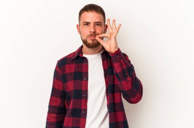 Diasteması olan beyaz tenli genç bir adam beyaz arka planda izole edilmiş ve parmakları dudaklarında bir sır saklıyor..