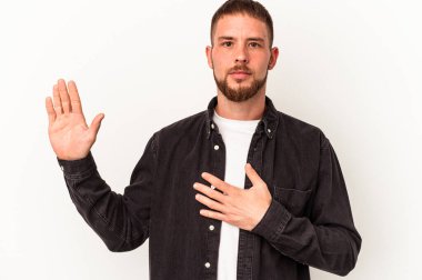 Beyaz arka planda izole edilmiş beyaz tenli genç beyaz adam yemin ediyor, elini göğsüne koyuyor..