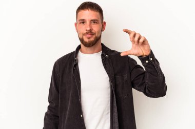 Diasteması olan beyaz tenli genç bir adam beyaz arka planda izole edilmiş. Elinde işaret parmaklarıyla küçük bir şey tutuyor, gülümsüyor ve kendinden emin..