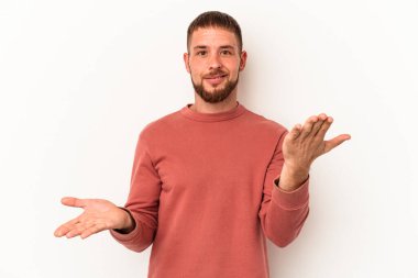 Beyaz arka planda izole edilmiş beyaz tenli genç beyaz adam kollarıyla ölçek oluşturuyor, mutlu ve kendinden emin hissediyor..