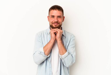 Beyaz arka planda izole edilmiş beyaz tenli genç beyaz adam ellerini çenesinin altında tutuyor ve mutlu bir şekilde yan tarafa bakıyor..