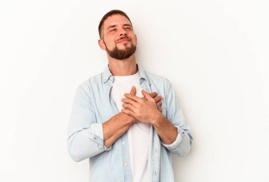 Beyaz arka planda izole edilmiş beyaz tenli genç beyaz adam gülüyor, ellerini kalbe koyuyor, mutluluk kavramını koruyor..