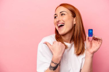 Pembe arka plan noktalarında pil tutan beyaz bir kadın. Baş parmak uzakta, gülen ve kaygısız..