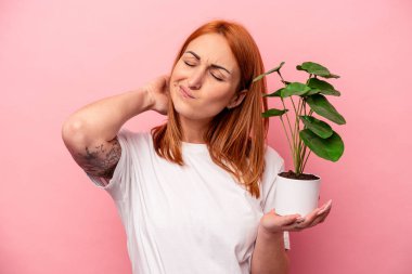 Pembe arka planda saklanmış bir bitki tutan beyaz bir kadın pembe arka planda izole edilmiş bir bitki tutan genç beyaz bir kadın kafasının arkasına dokunuyor ve bir seçim yapıyor..