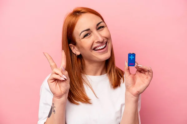 ピンクを基調としたバッテリーを持つ若い白人女性が喜びと屈託のない指で平和のシンボルを示す — ストック写真