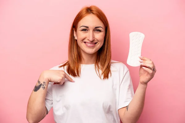 ピンクの背景に隔離された生理用ナプキンを持っている若い白人女性シャツのコピースペースに手で指して 誇りと自信 — ストック写真