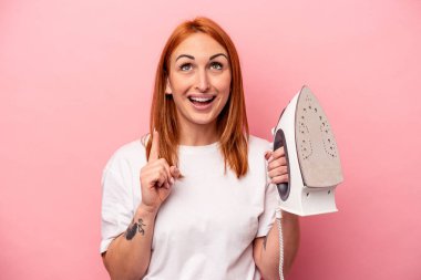 Pembe arka planda demir tutan beyaz bir kadın ağzı açık bir şekilde üst tarafı işaret ediyor..