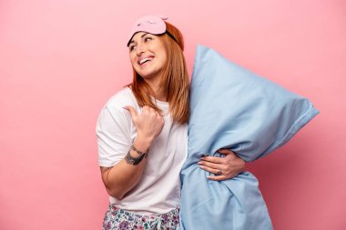 Pembe arka plan noktalarına izole edilmiş pijama tutan beyaz bir kadın başparmağıyla gülüyor ve kaygısız..