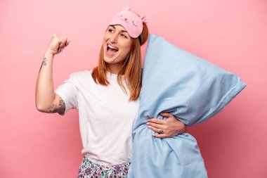 Pembe arka planda izole edilmiş pijama giyen beyaz bir kadın zafer kazandıktan sonra yumruğunu kaldırıyor..