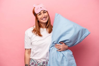 Pembe arka planda izole edilmiş pijama giyen beyaz bir kadın mutlu, gülümseyen ve neşeli..