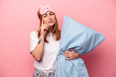 Pembe arka planda izole edilmiş pijama giyen beyaz bir kadın şakağı parmağıyla göstererek bir göreve odaklanmış..