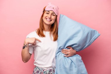 Pembe arka plandaki izole edilmiş pijama giyen beyaz bir kadın gömlek fotokopi odasını işaret ediyor, gururlu ve kendinden emin.