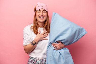 Pembe arka planda izole edilmiş pijama giyen beyaz kadın kahkahalar atıyor ve elini göğsüne koyuyor..