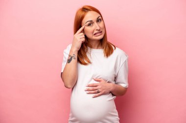 Pembe arka planda izole edilmiş beyaz hamile bir kadın işaret parmağıyla hayal kırıklığı jesti yapıyor..