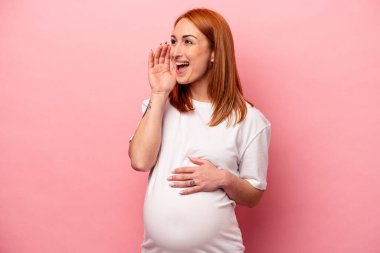 Genç beyaz hamile kadın pembe arka planda izole edilmiş bağırıyor ve avuç içini açık tutuyor..