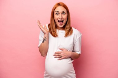 Pembe arka planda izole edilmiş beyaz hamile kadın şaşırdı ve şok oldu..