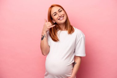 Pembe arka planda izole edilmiş genç beyaz kadın parmaklarıyla bir cep telefonu hareketi gösteriyor..