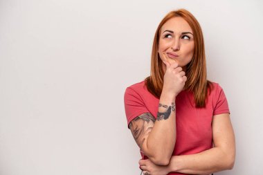 Beyaz arka planda soyutlanmış beyaz tenli genç bir kadın şüpheli ve şüpheci bir ifadeyle yana bakıyor..