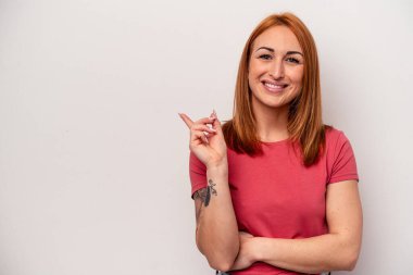 Beyaz arka planda izole edilmiş genç beyaz kadın işaret parmağıyla işaret ederek gülümsüyor..