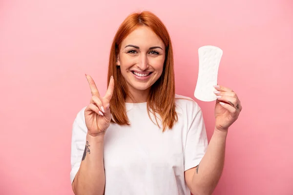 ピンクの背景に隔離された生理用ナプキンを持っている若い白人女性は指で2番目を示す — ストック写真