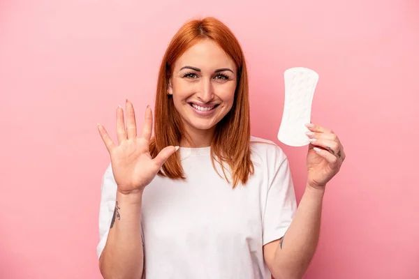 若いですCaucasian女性保持衛生ナプキン隔離上のピンクの背景笑顔陽気に示す番号5とともに指 — ストック写真