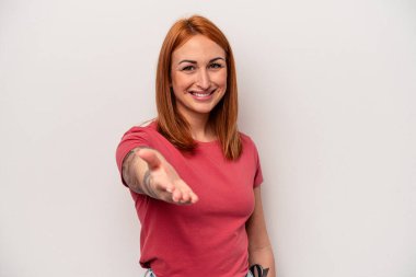 Beyaz arka planda izole edilmiş genç beyaz kadın selamlaşma jesti olarak kameraya elini uzatıyor..