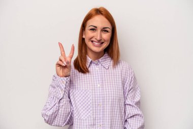 Beyaz arka planda izole edilmiş genç beyaz kadın neşeli ve kaygısız parmakları olan bir barış sembolü gösteriyor..